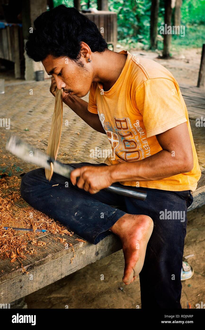 Attapu / Laos - JUL 06 2011: member of the local dragon boat team preparing for the competition by carving his own paddle (and later on they won the c Stock Photo