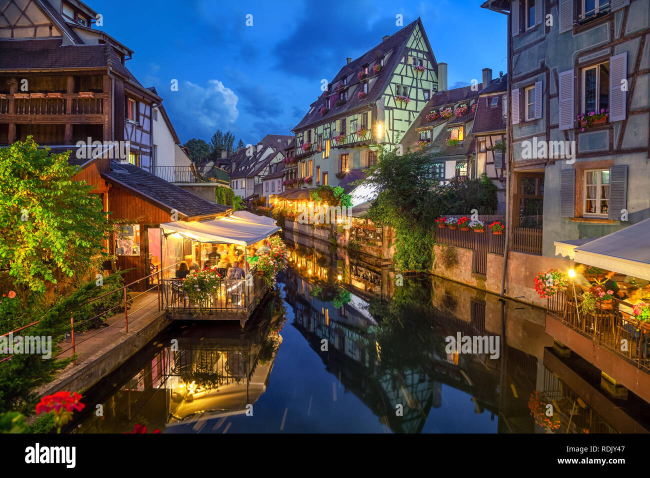 Colmar, France. Half-timbered houses and verandas of restaurants reflecting in the water at dusk in Petite Venise area Stock Photo