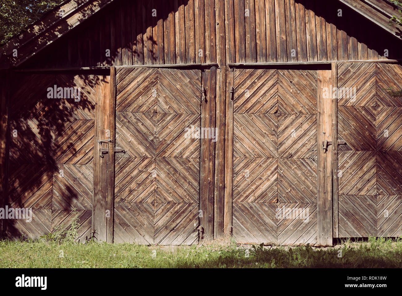 An aged, rural farm building with two doors and rusted locks with a rustic natural wooden facade and decorative woodwork in a creative pattern Stock Photo