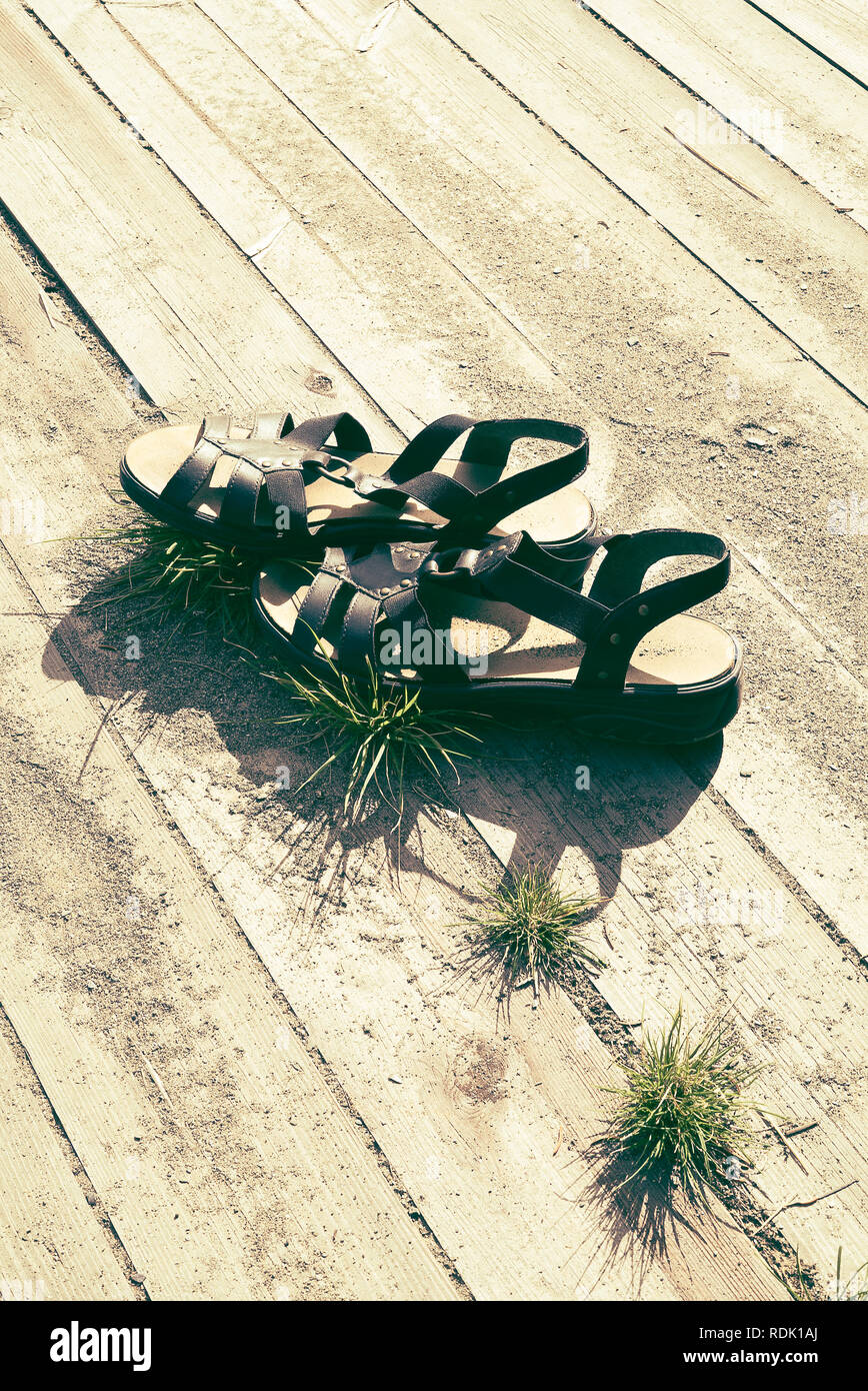 Woman summer sandals in  warm sunshine on wooden planks with sand and grass, with free empty space for copy - Concept of relaxing vacation, summertime Stock Photo