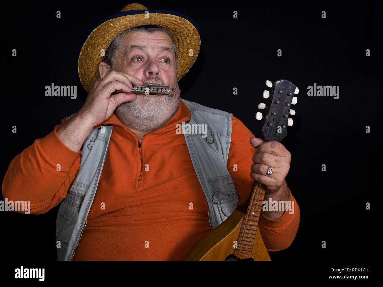 Senior musician playing mouth-organ while holding mandolin Stock Photo