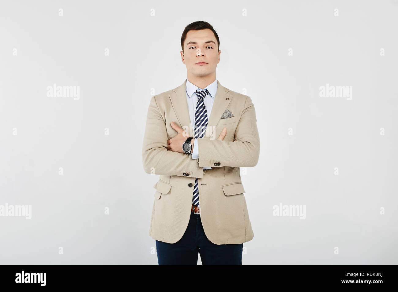 Stylish and handsome young brunet man in the white shirt with striped tie, in a beige blazer and in dark jeans posing at white background, isolated Stock Photo