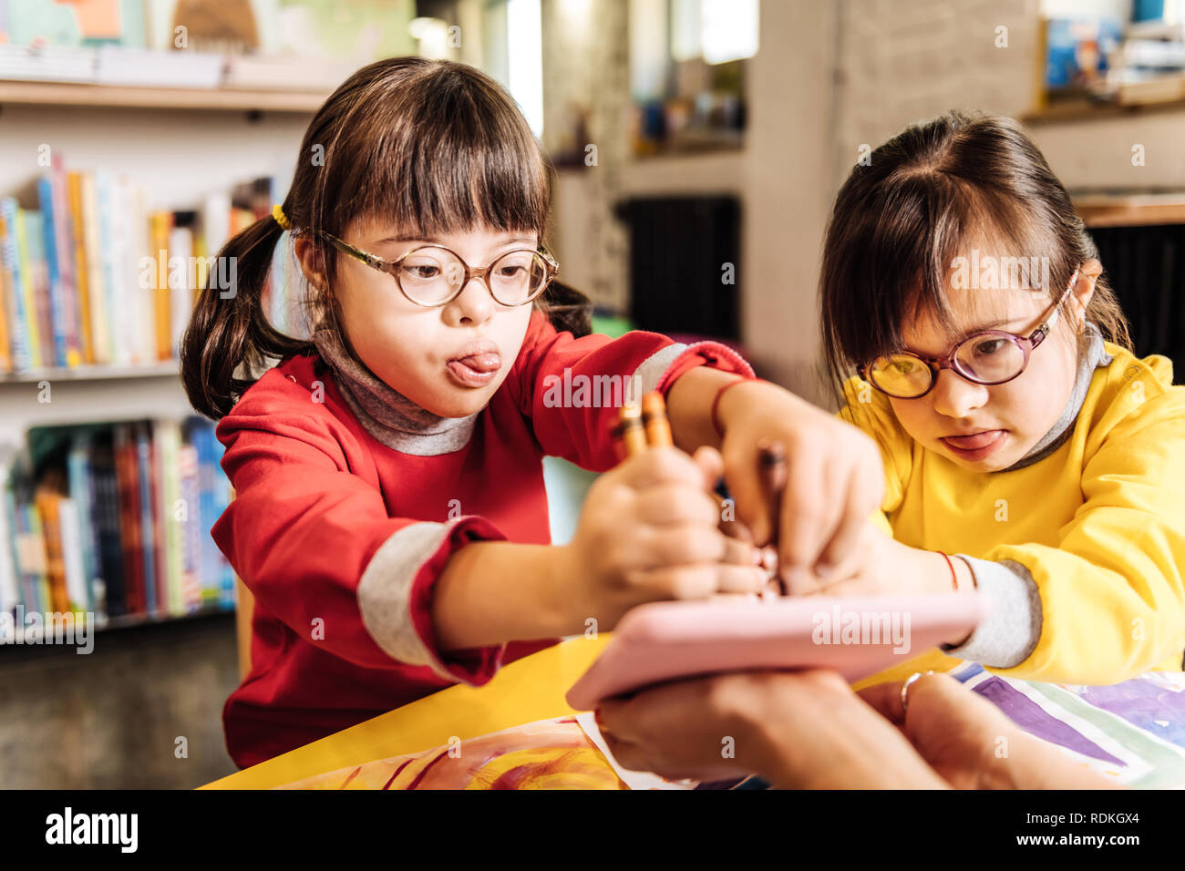 Cute lovely sisters with chromosome abnormality drawing with crayons Stock Photo