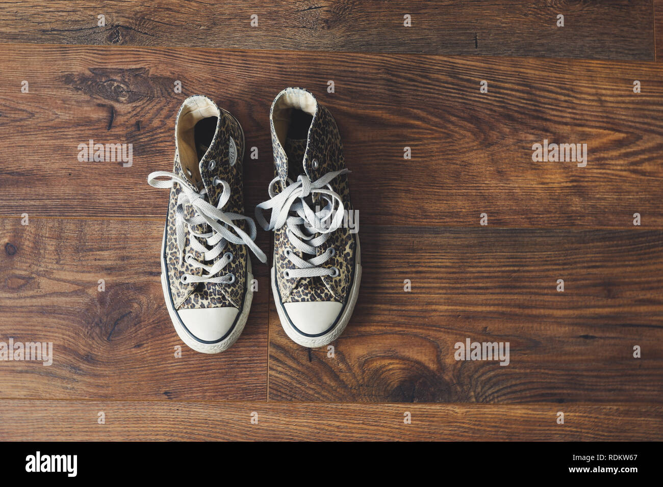 Converse all star shoes / trainers with an animal print, photographed against wooden floor Stock Photo