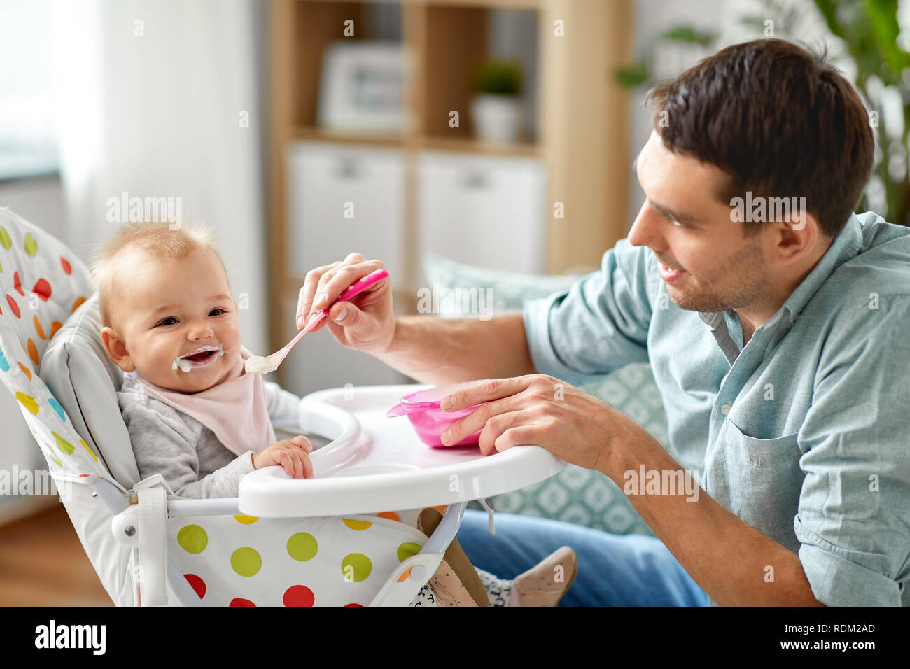 father feeding happy baby in highchair at home Stock Photo