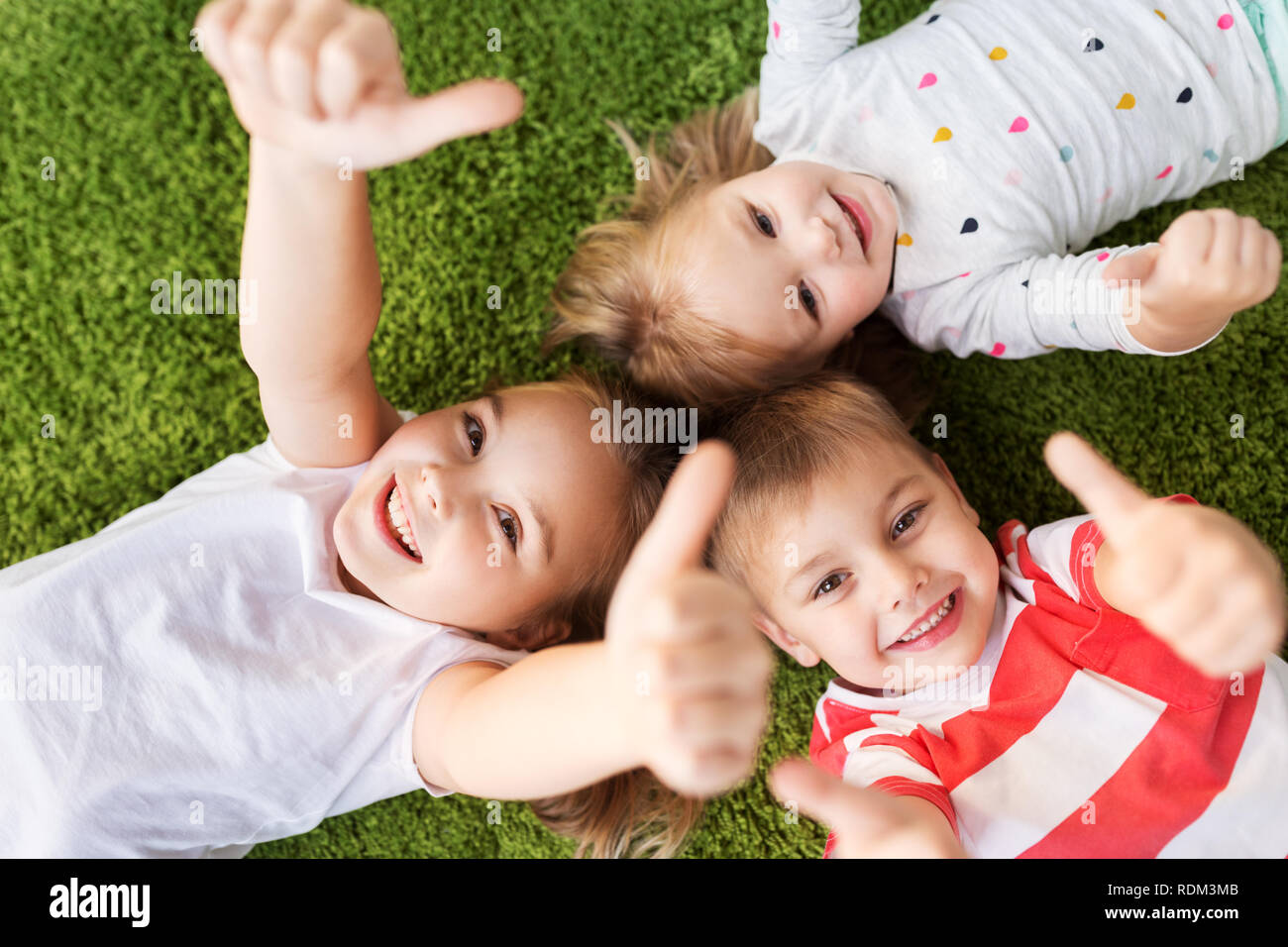 happy kids lying on floor and showing thumbs up Stock Photo - Alamy