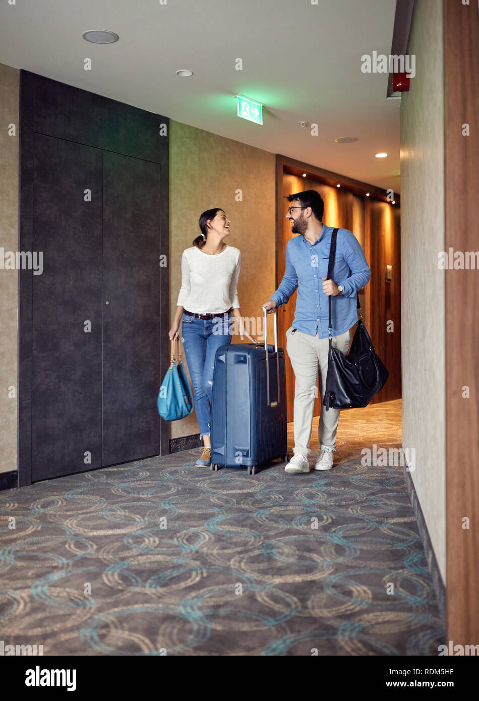Smiling man and woman arriving at hotel lobby with suitcase Stock Photo