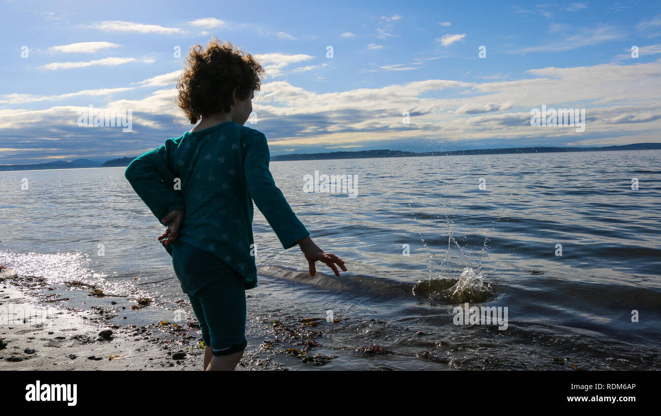 young child throwing rock into Pugeot Sound at Alki Beach waterfront in West Seattle, WA Stock Photo
