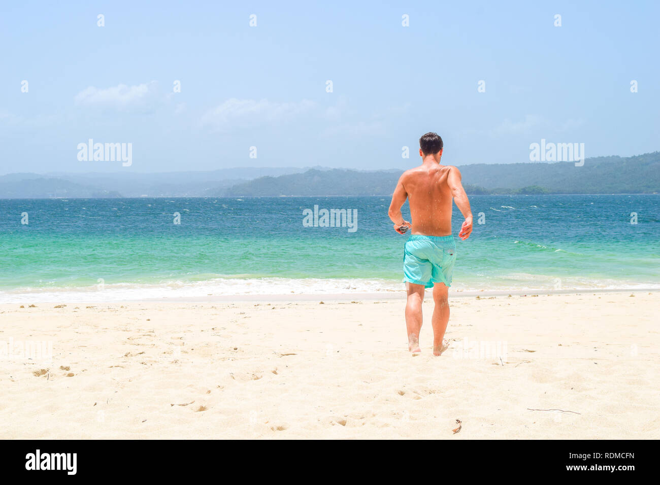 Man running barefoot on the beach into the turquoise ocean on an island, caribbean sea Stock Photo