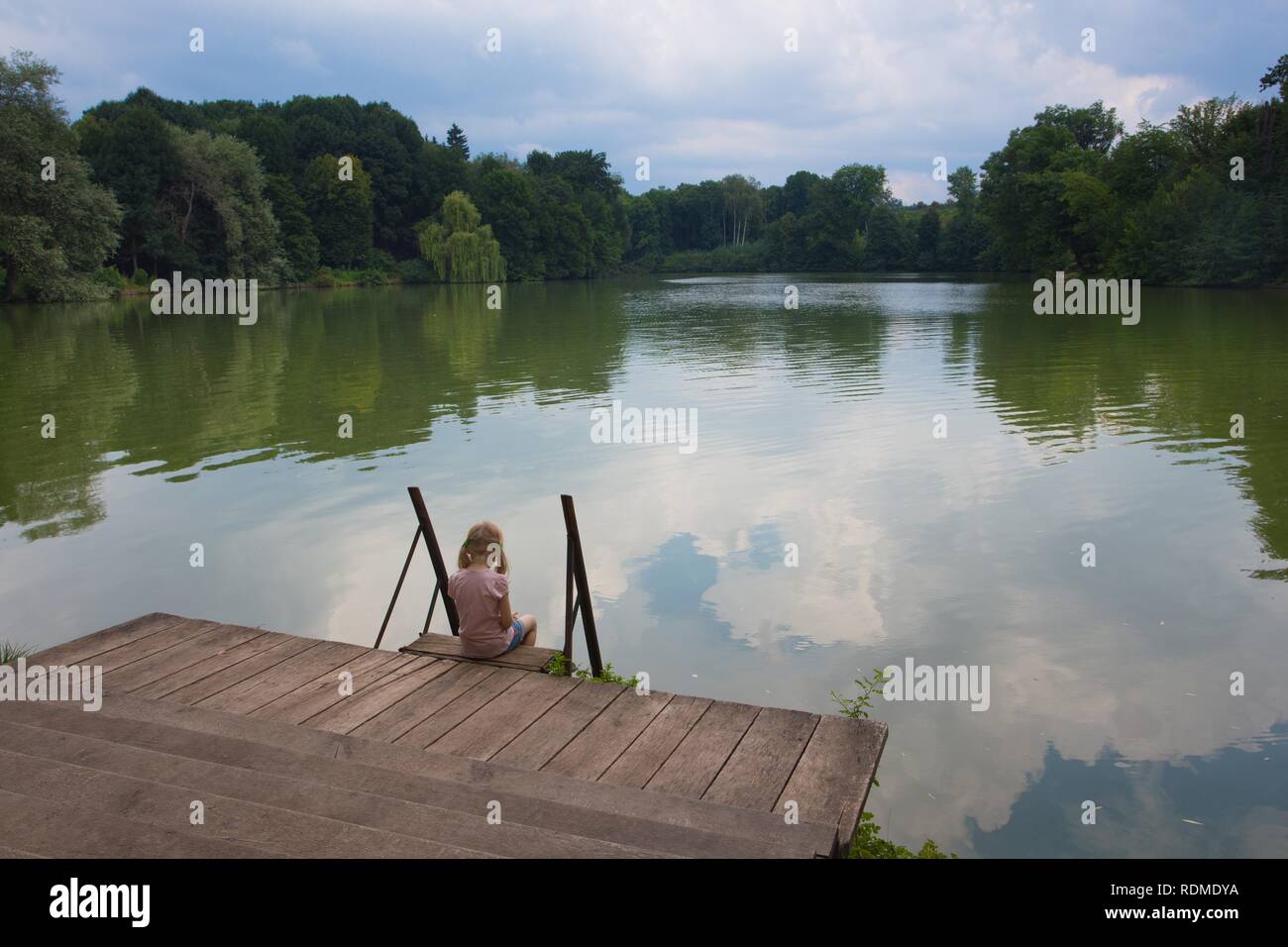 sad little girl sitting on a river bank Stock Photo - Alamy