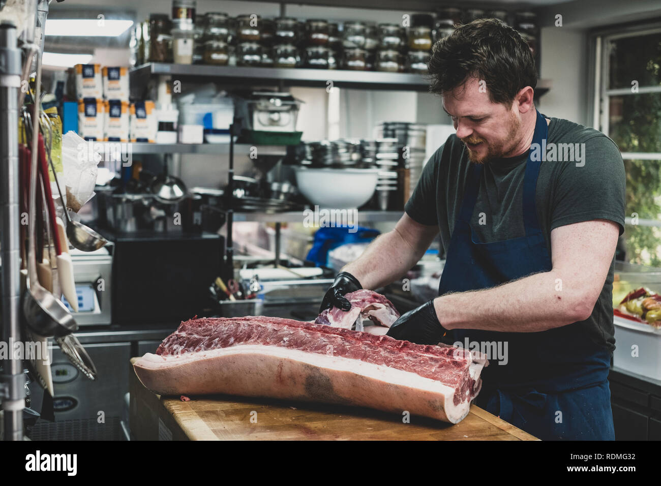 Male butcher wearing apron and black rubber gloves cutting pork ribs on