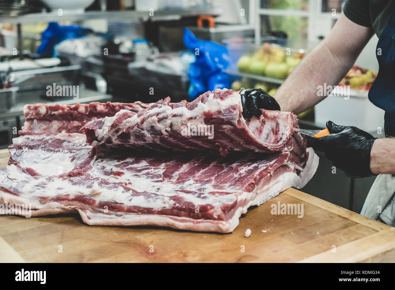 Close up of butcher wearing black rubber gloves cutting pork ribs on butcher's block. Stock Photo