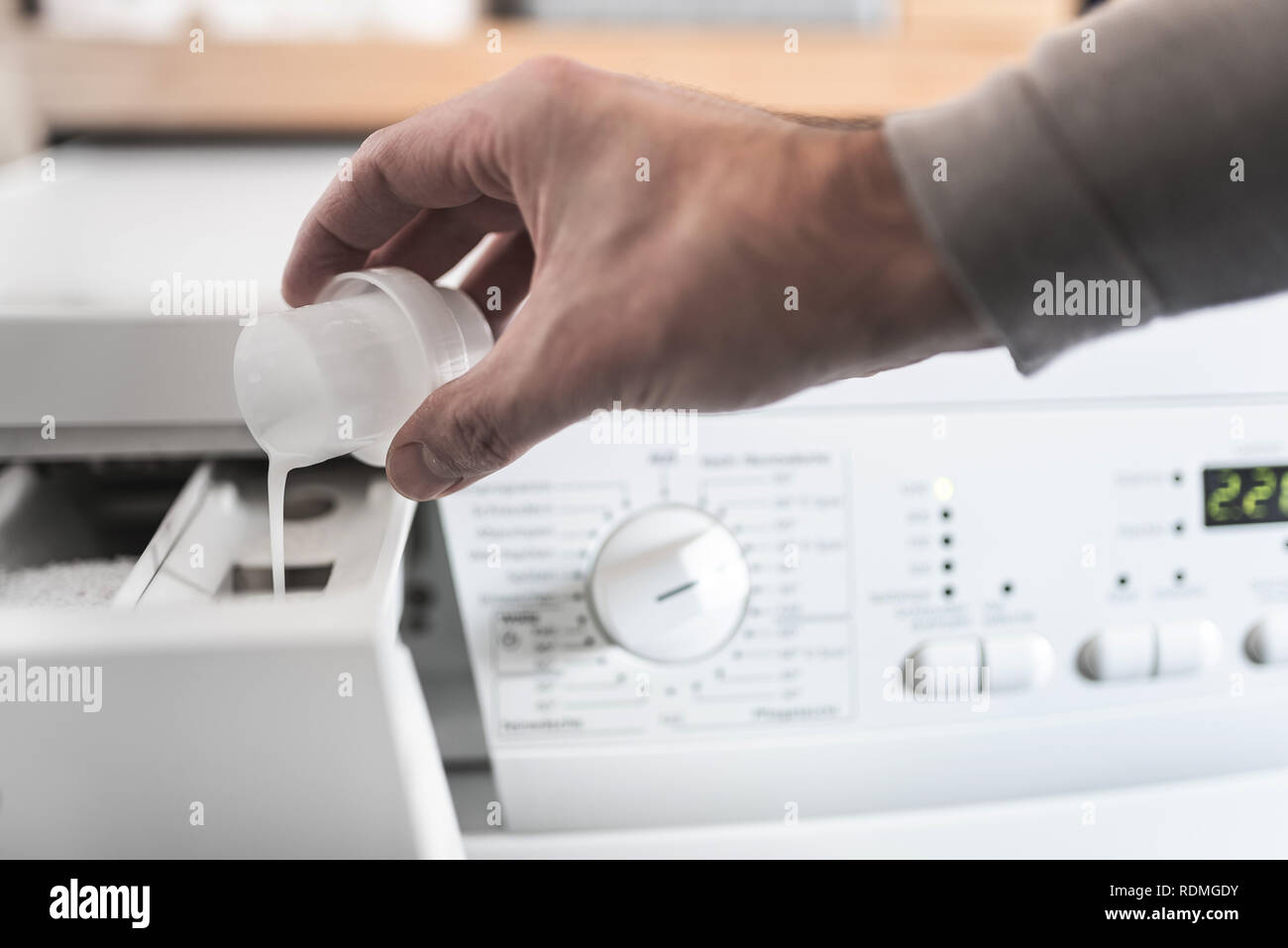 person using dosing aid to fill fabric softener into washing machine Stock Photo