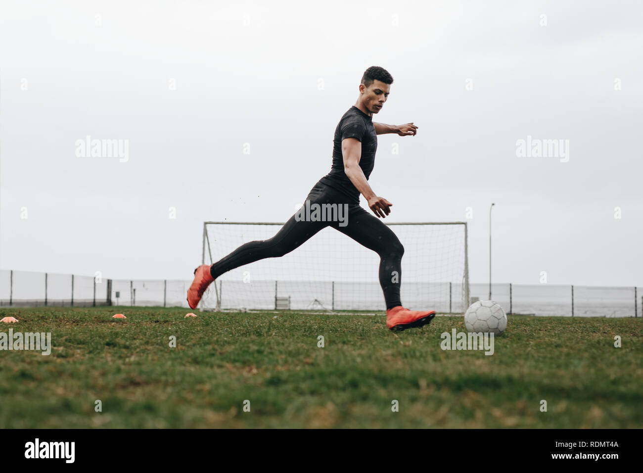 Soccer player in position to kick a football. Footballer practicing his game on field early in the morning. Stock Photo