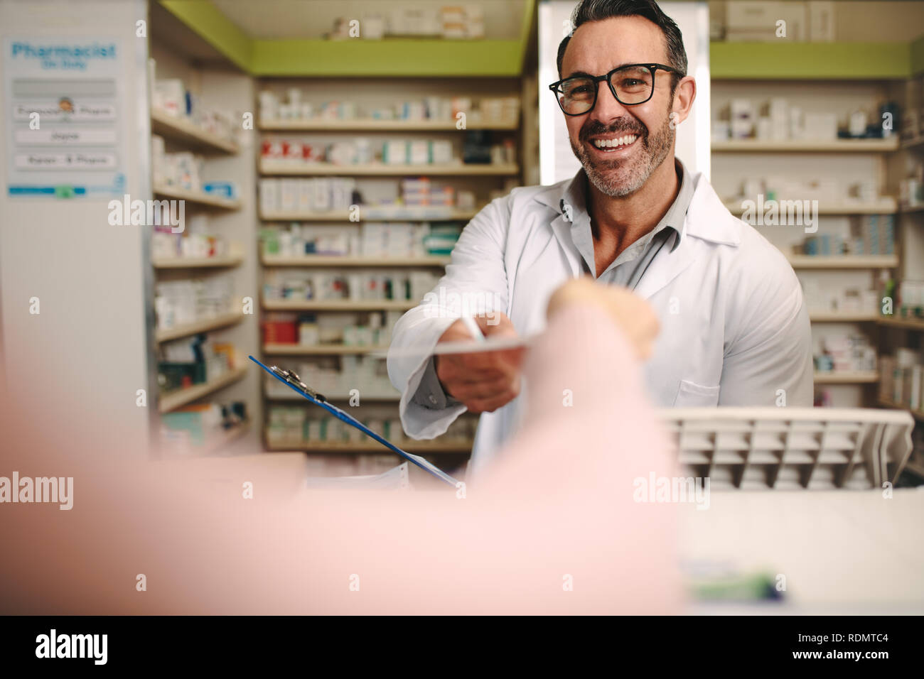 Male apothecary taking prescription from customer at pharmacy. Customer handing a medical prescription to the chemist standing behind counter. Stock Photo