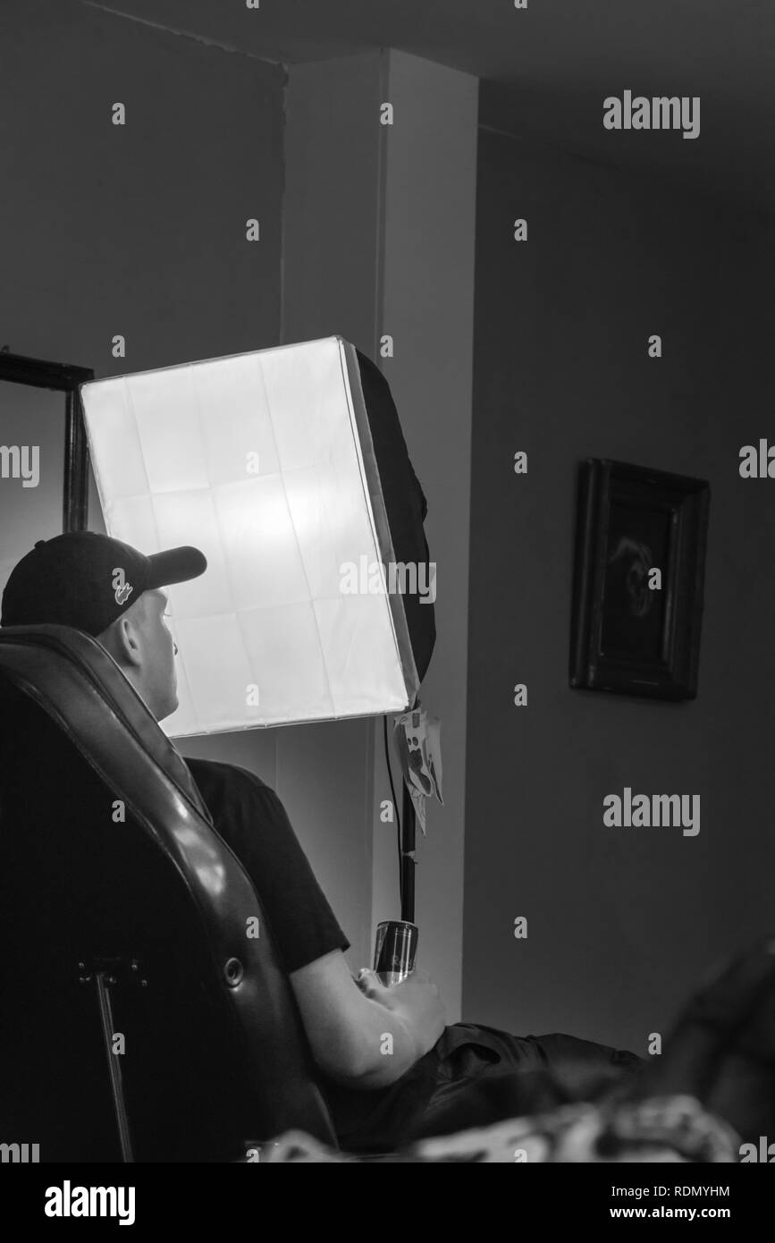 young man sitting in a chair with a can in his hand with a soft-box studio lamp in front of him Stock Photo