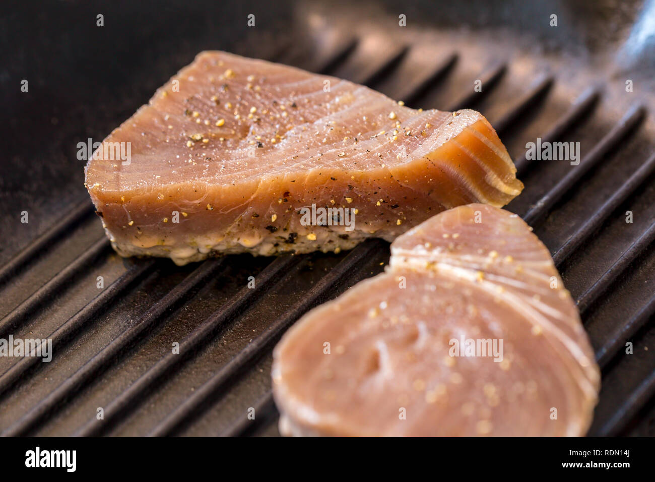 Close up of chargrilled tuna steaks cooking in a griddle pan with