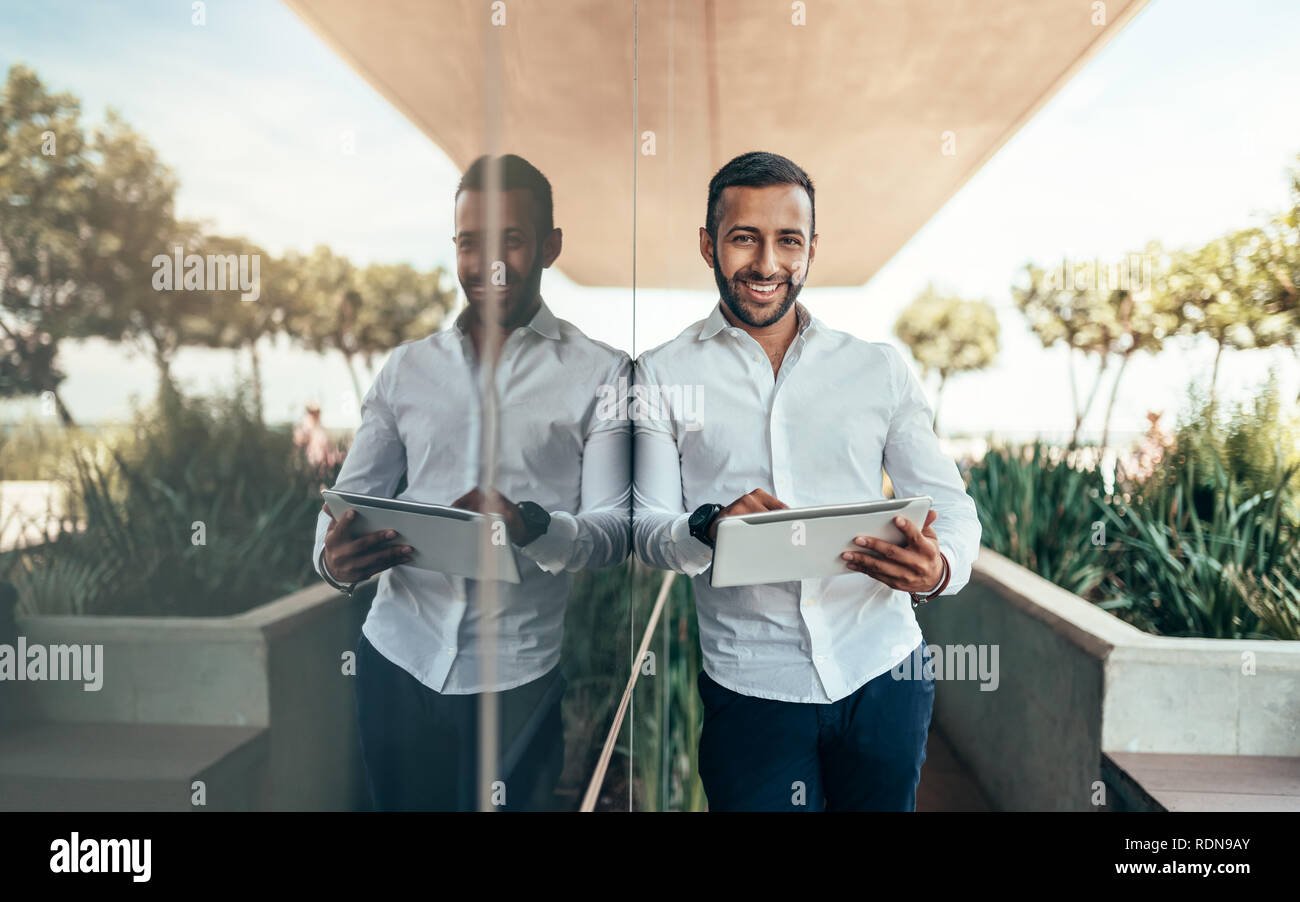 Indian man standing next to glass building with reflection Stock Photo