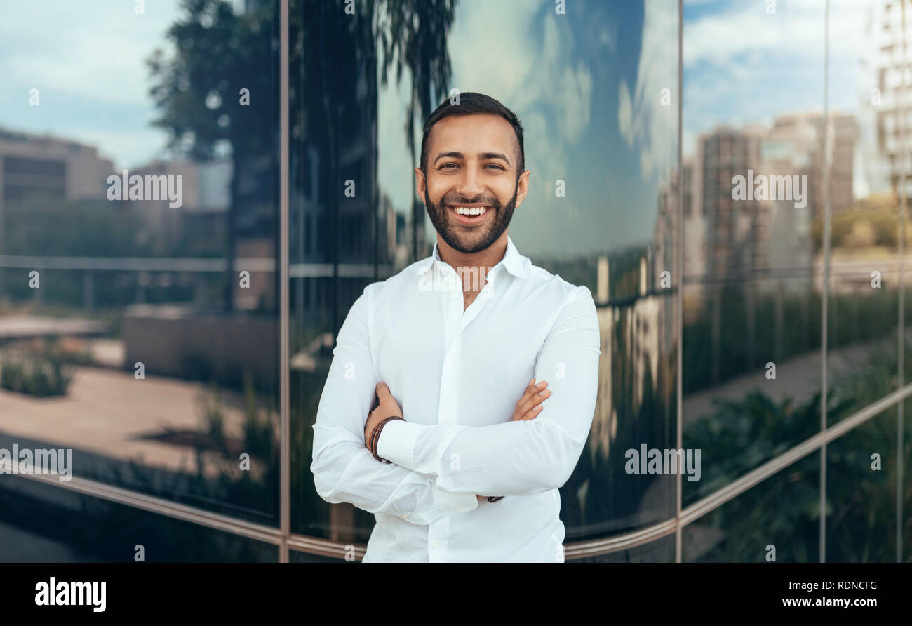 Portrait of a young confident smiling indian man with his arms crossed ...
