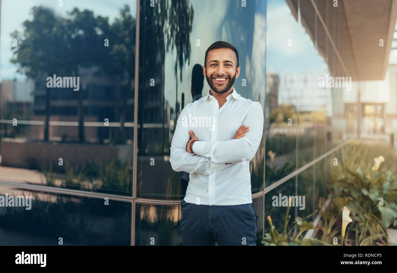 Portrait of a young confident smiling indian man with his arms crossed ...