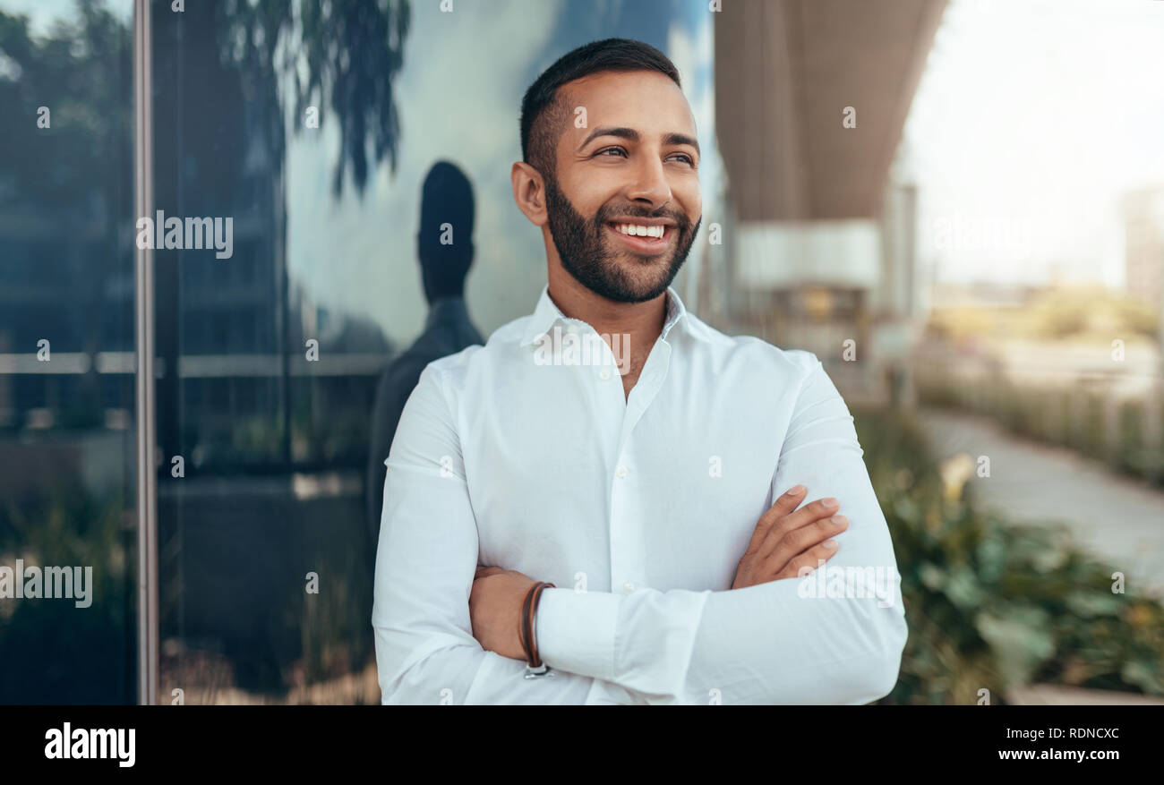 Portrait of a young confident smiling indian man with his arms crossed ...