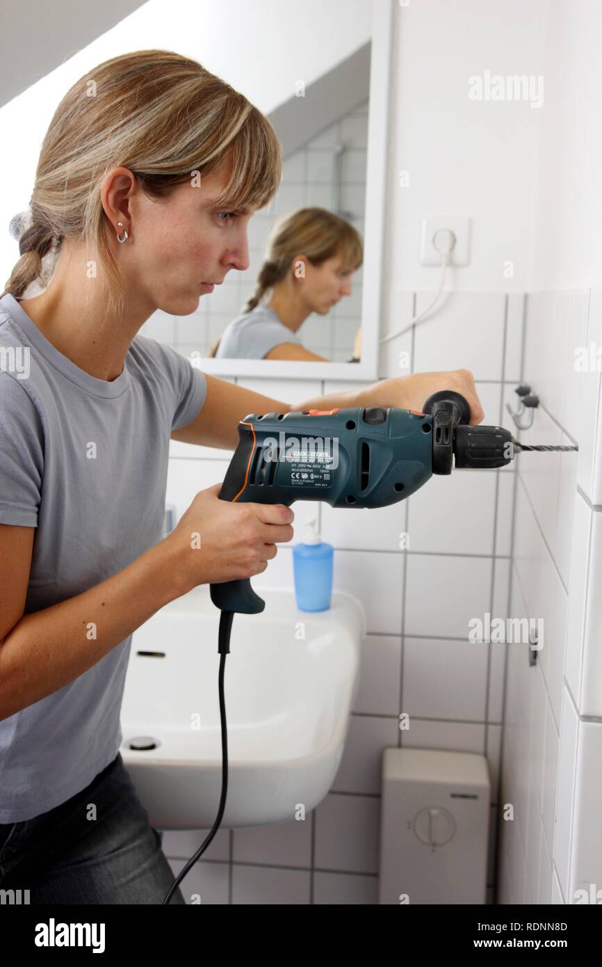 Young woman drilling a hole into a tiled bathroom wall Stock Photo Alamy