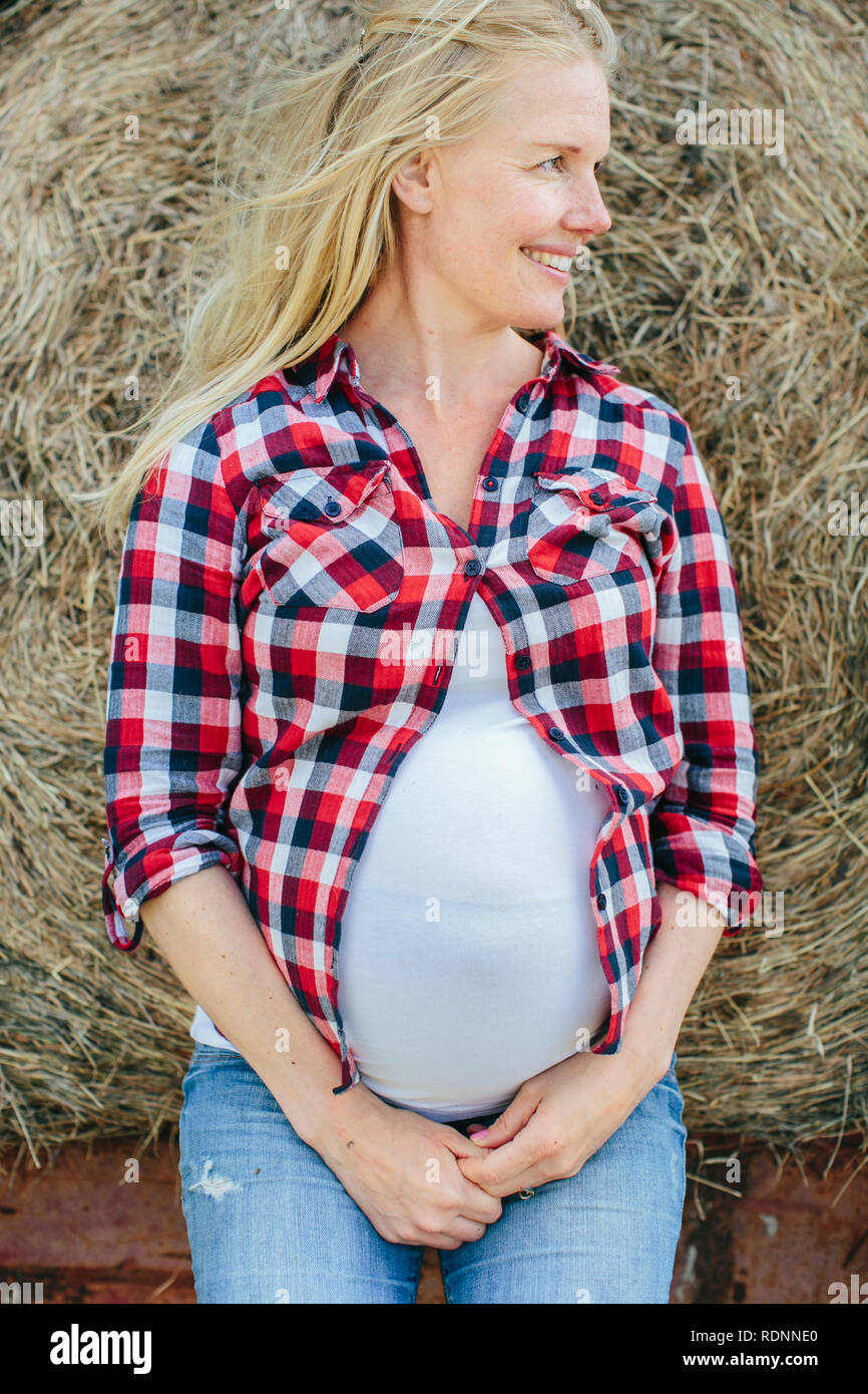 Pregnant woman leaning on haybale Stock Photo