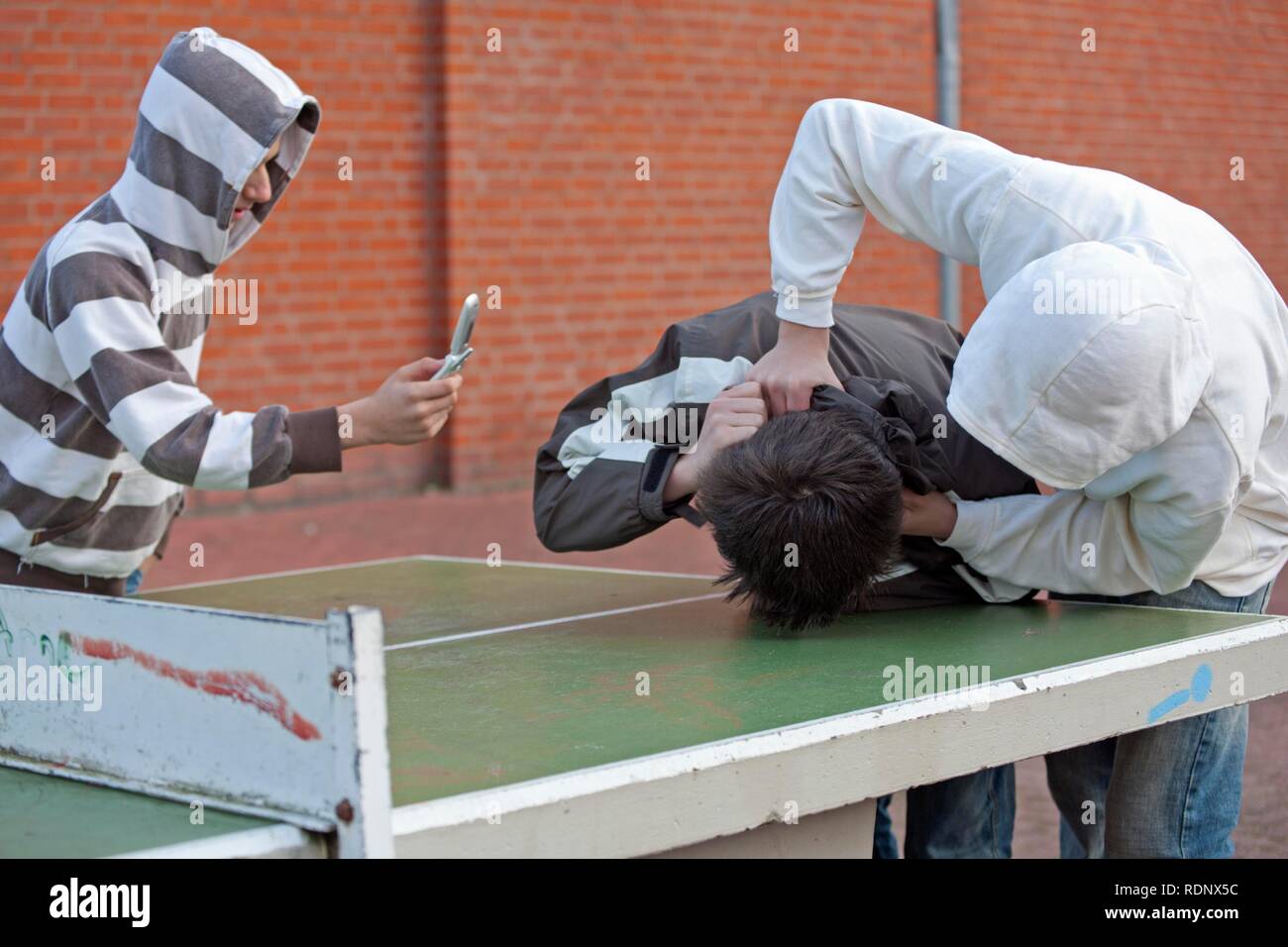 Two boys fighting on the playground while a third films with his cell phone, posed scene Stock Photo