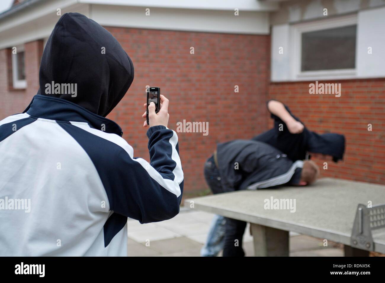 Boy being beaten on the playground while a third films with his cell phone, posed scene Stock Photo