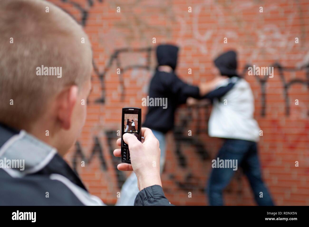 Two boys fighting on the playground while a third films with his cell phone, posed scene Stock Photo
