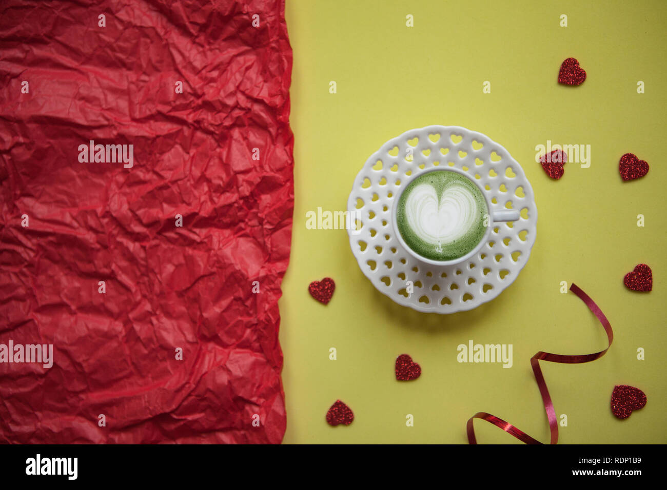 A cup with a tasty and aromatic morning matcha latte coffee on a festive background with many hearts. Next to a red background there is a place for text. Celebration of Valentine's Day or Women's Day or other love event. Stock Photo