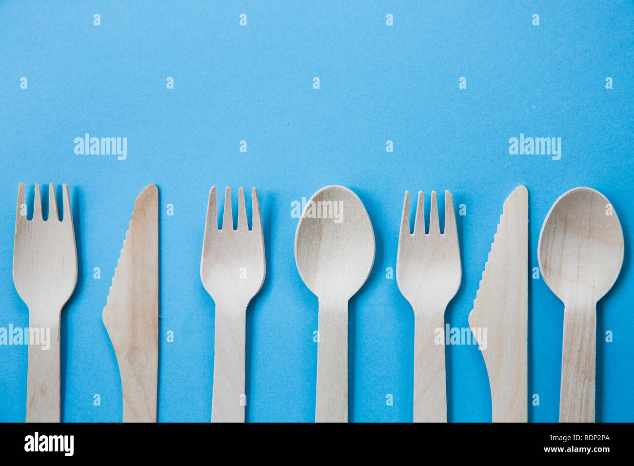A variety of recyclable wooden cutlery including knife, fork and spoon on a blue background Stock Photo