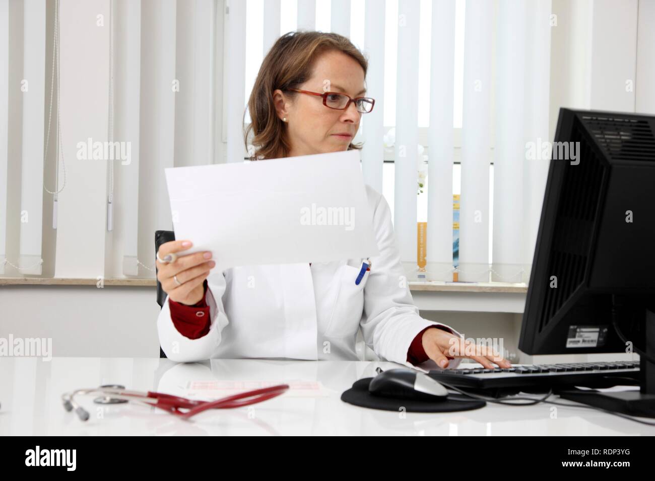 Medical practice, doctor examining the health records of a patient at her desk Stock Photo