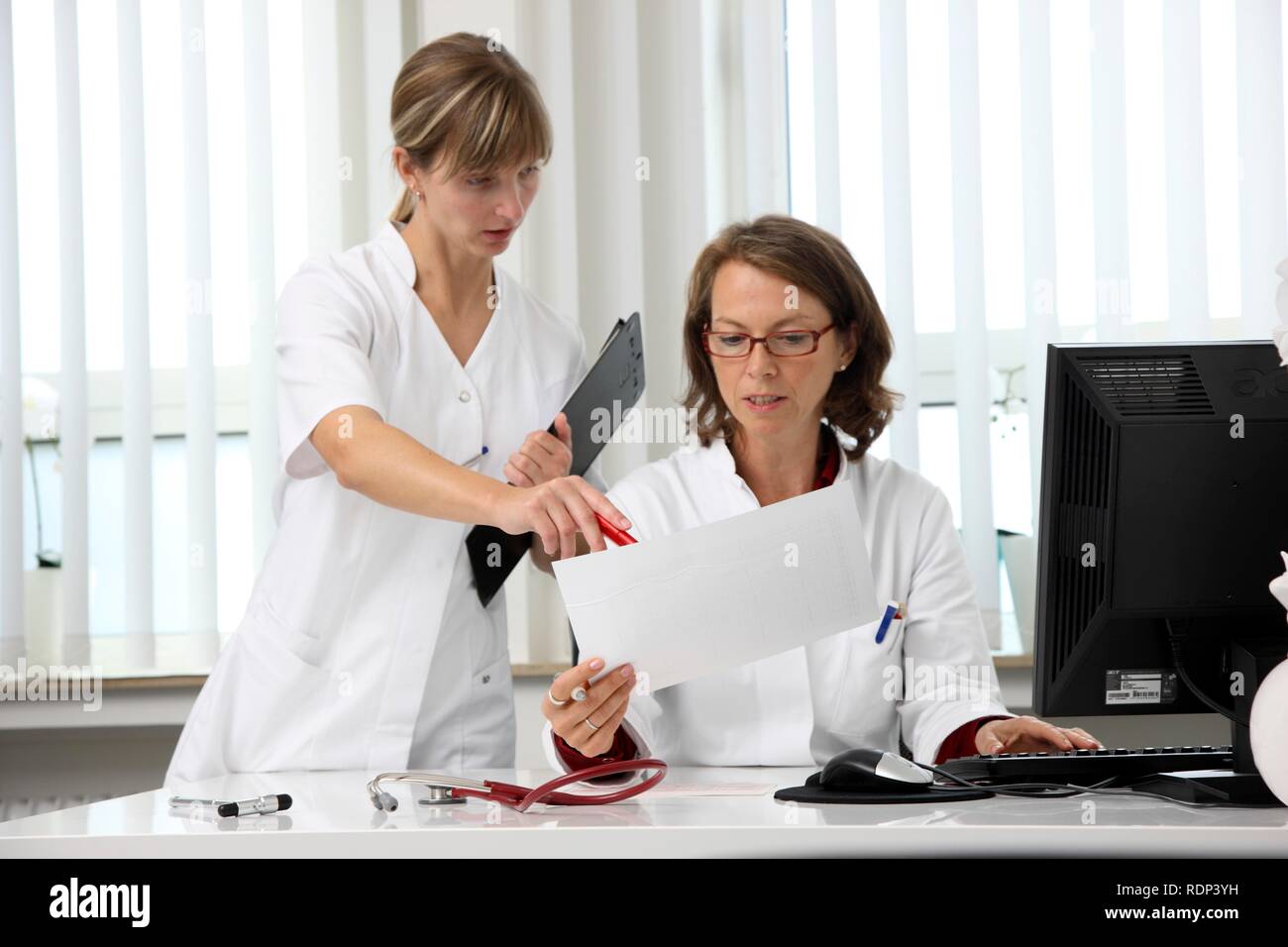 Medical practice, doctor examining the health records of a patient at her desk, discussing them with an assistant Stock Photo