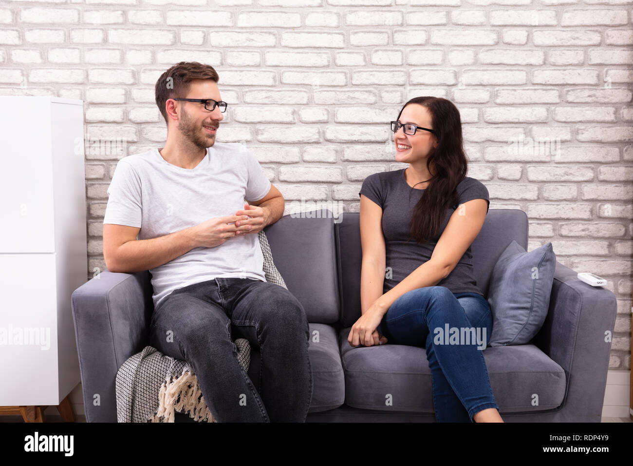 Young Men And Woman Sitting On Sofa Looking At Each Other During Date Stock Photo