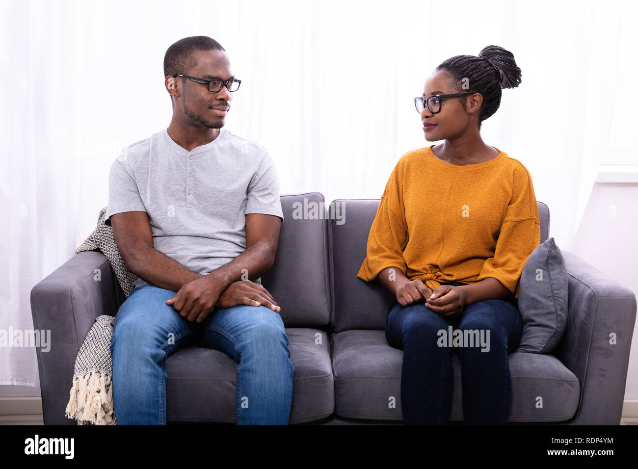 An African Young Couple Sitting On Sofa Looking At Each Other Stock Photo