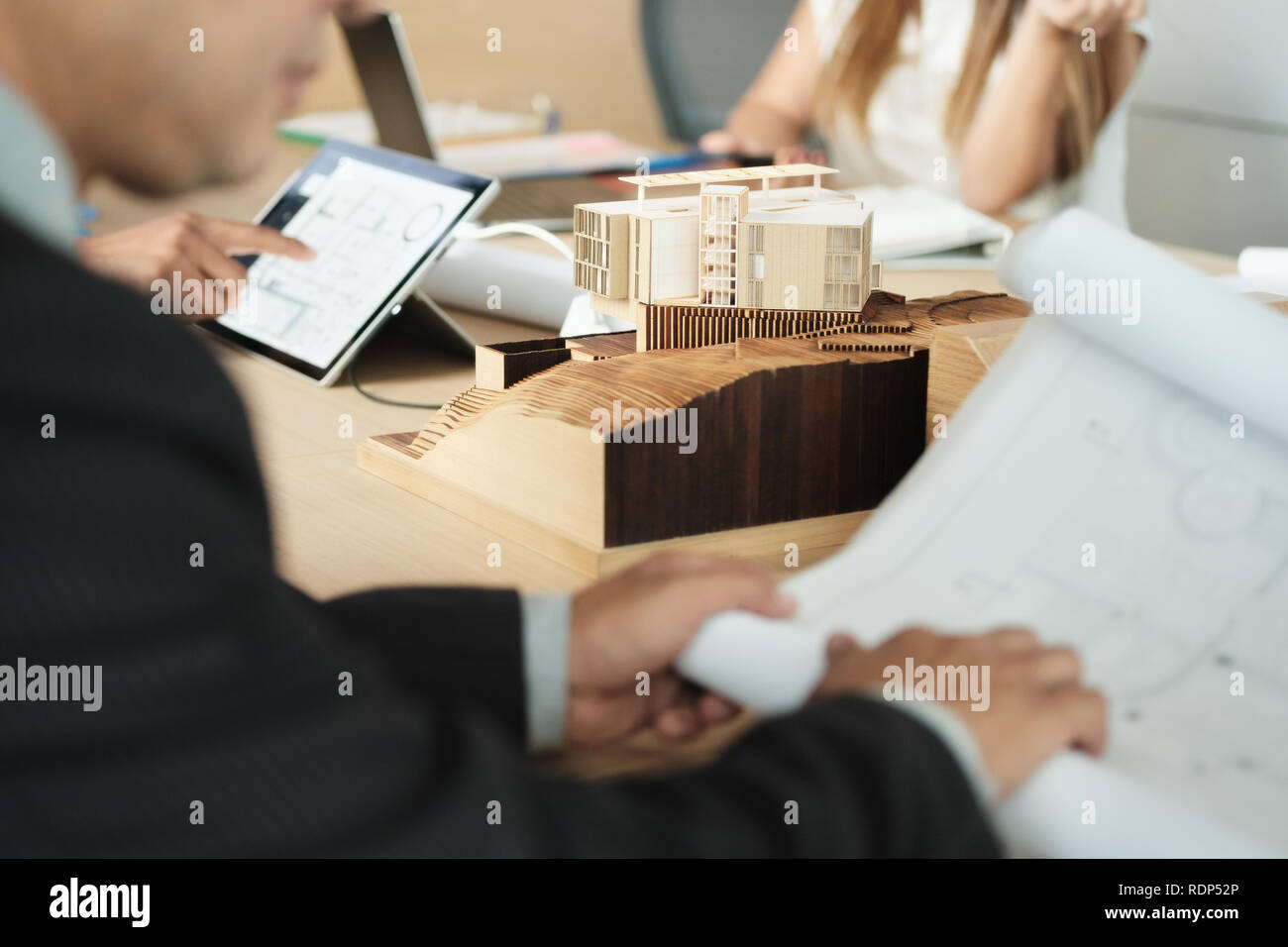 Miniature Building At Business Meeting With Architect Looking at Blueprints Stock Photo