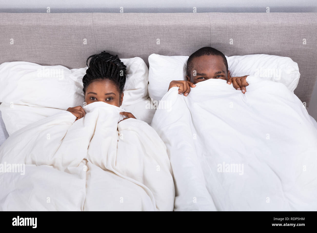 High Angle View Of An African Couple Trying To Hide In Blanket Stock Photo