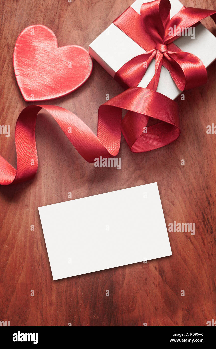 White gift box and red ribbon with tag on wood background with space. Vintage gift box on wooden board with space for text. Stock Photo