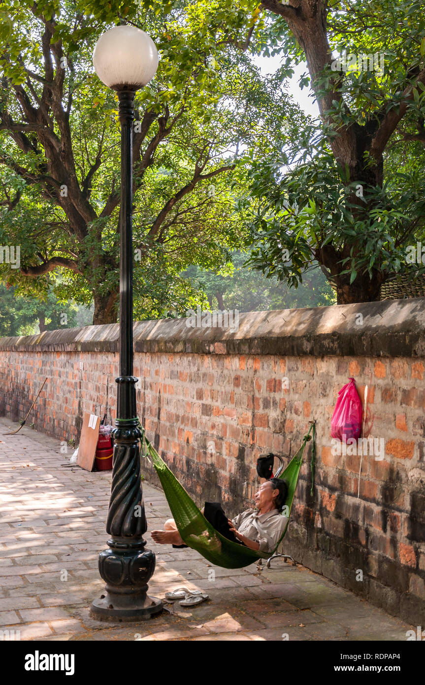A Vietnamese man sleeping in a makeshift hammock against a lamp post and a wall, Hanoi, Vietnam Stock Photo