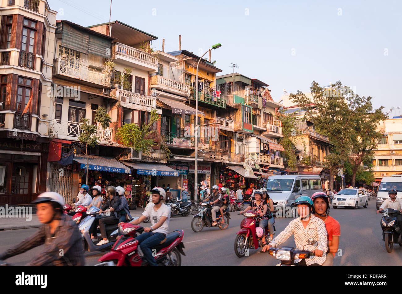 Busy intersection with several cars, mopeds and motorbikes on the road in afternoon light, Hanoi, Vietnam Stock Photo