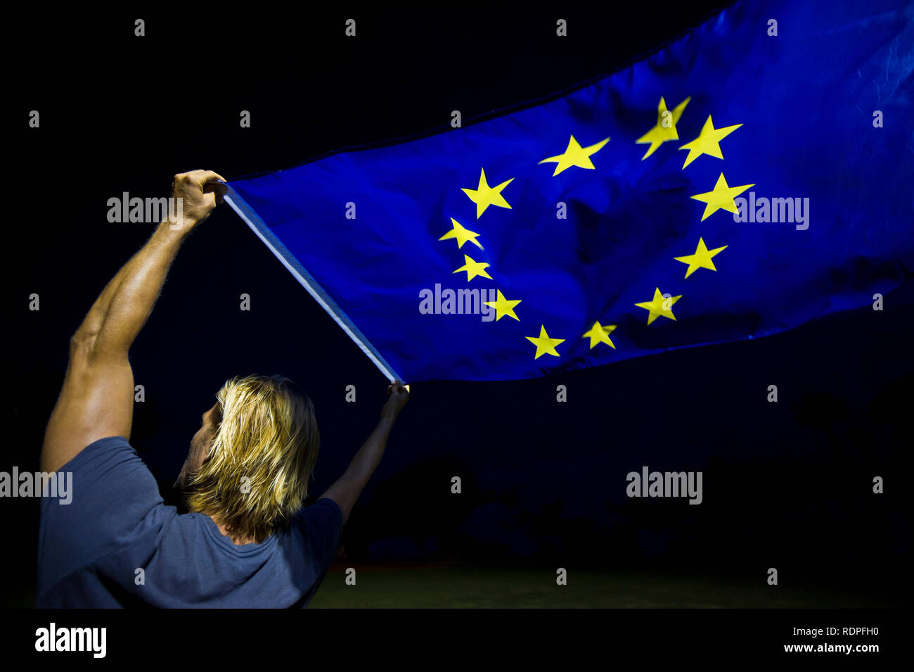 Man with blond hair holding a European Union flag waving against black night sky Stock Photo
