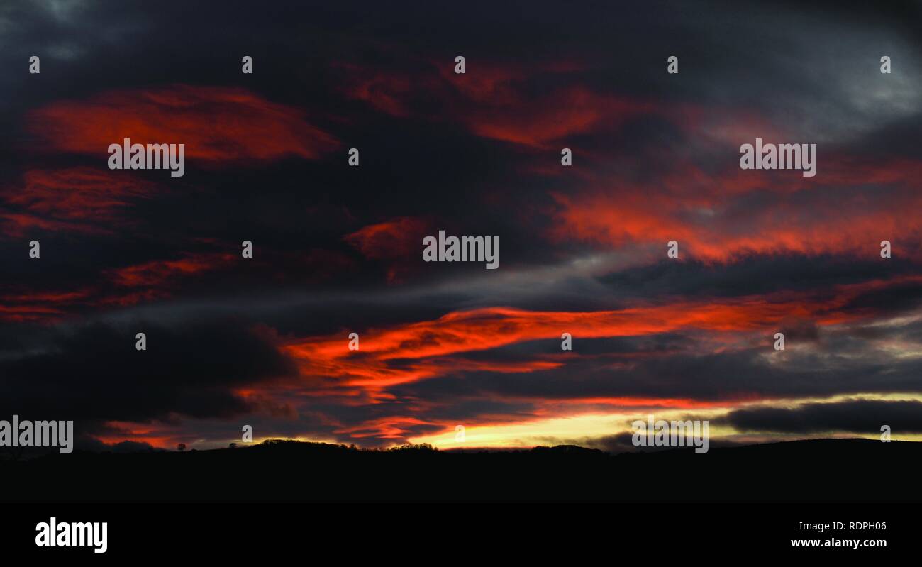 Stunning sunset with red clouds against a storm grey sky. Over Dartmoor, Devon. Stock Photo