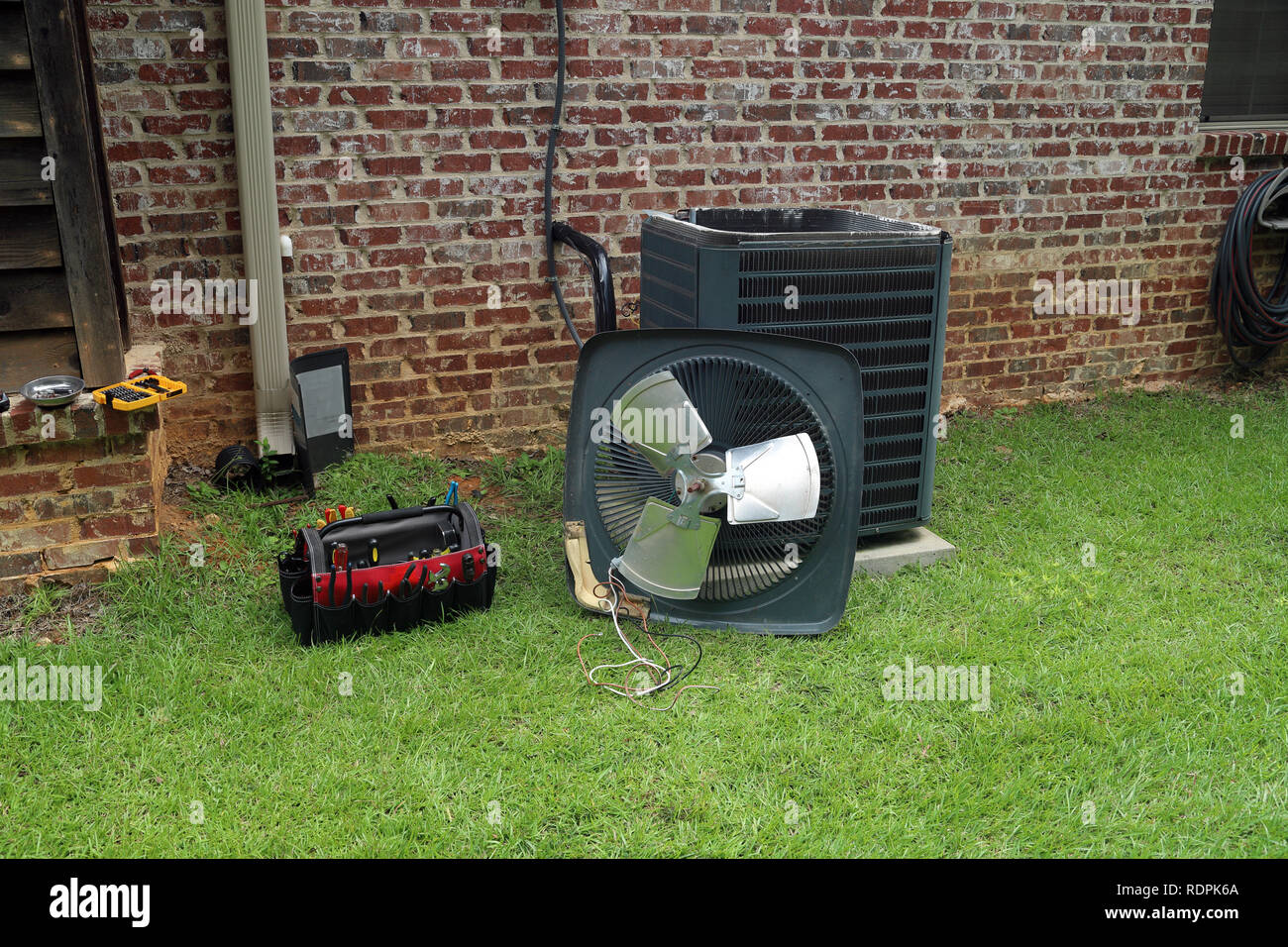 Air Conditioner compressor condenser coil with fan and tools being worked on next to a brick house for repair maintenance. Stock Photo