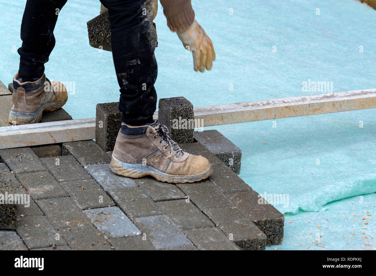 Construction worker laying interlocking paving concrete onto sheet