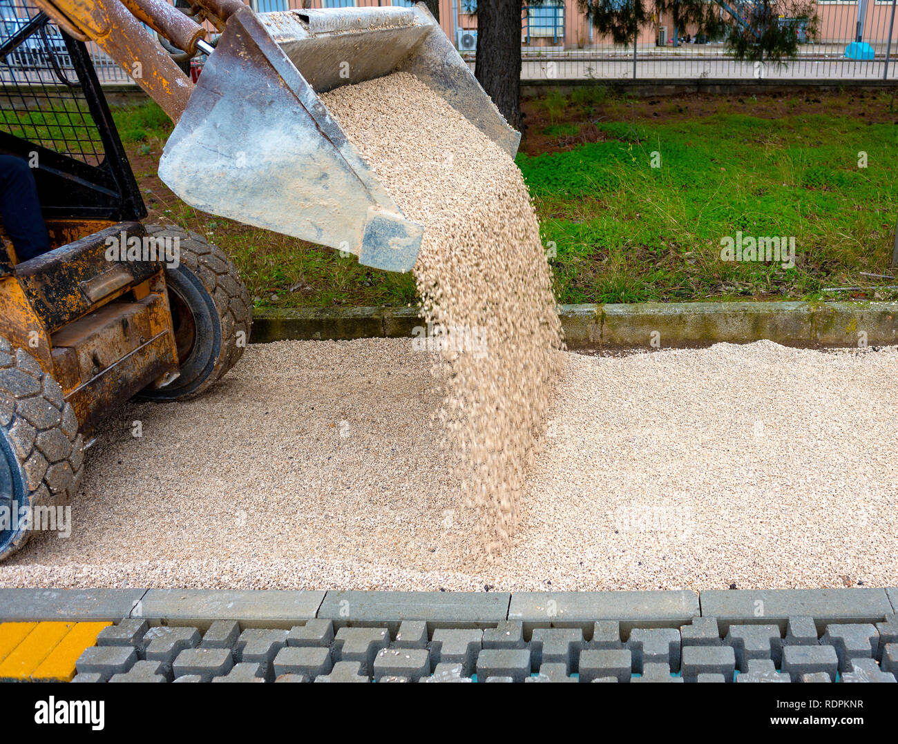 skid loader distributes grit and sand for the background of the pavement paving Stock Photo