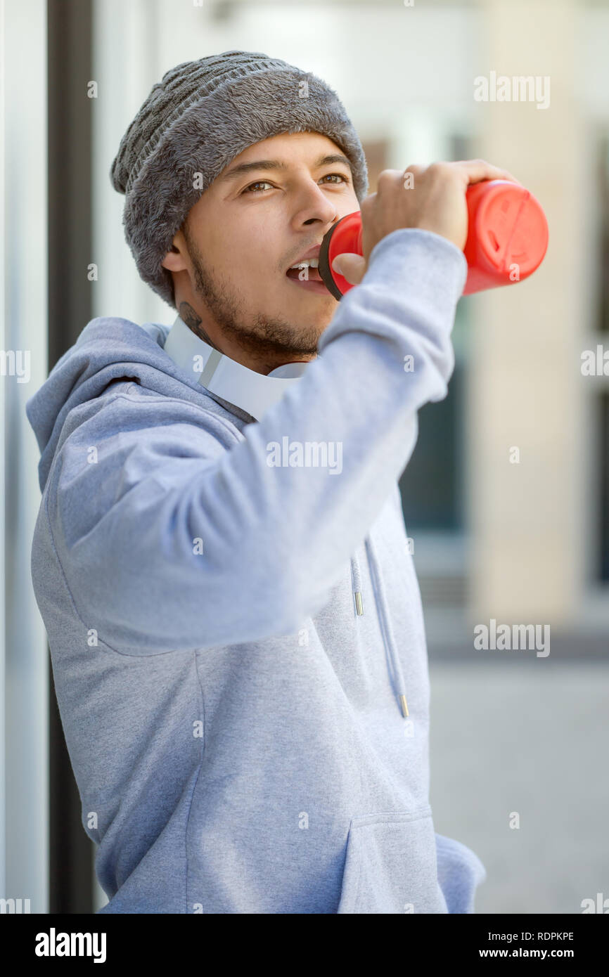 Sports training young latin man drinking water looking up thinking portrait format runner outdoor Stock Photo