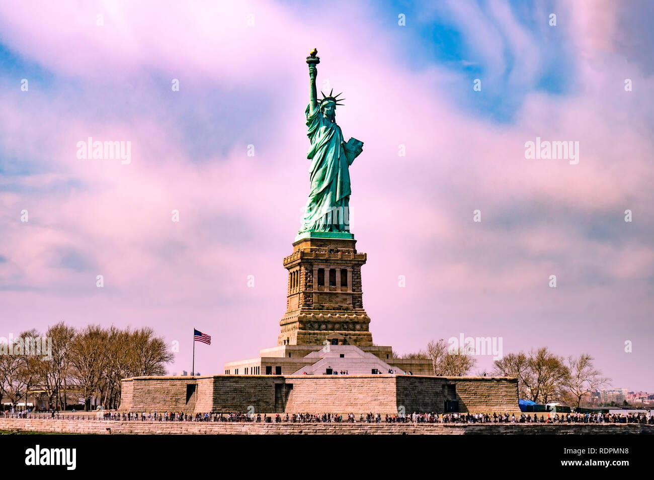 Statue of liberty in the middle with many tourists around it with pinky cloudy sky before sunset Stock Photo