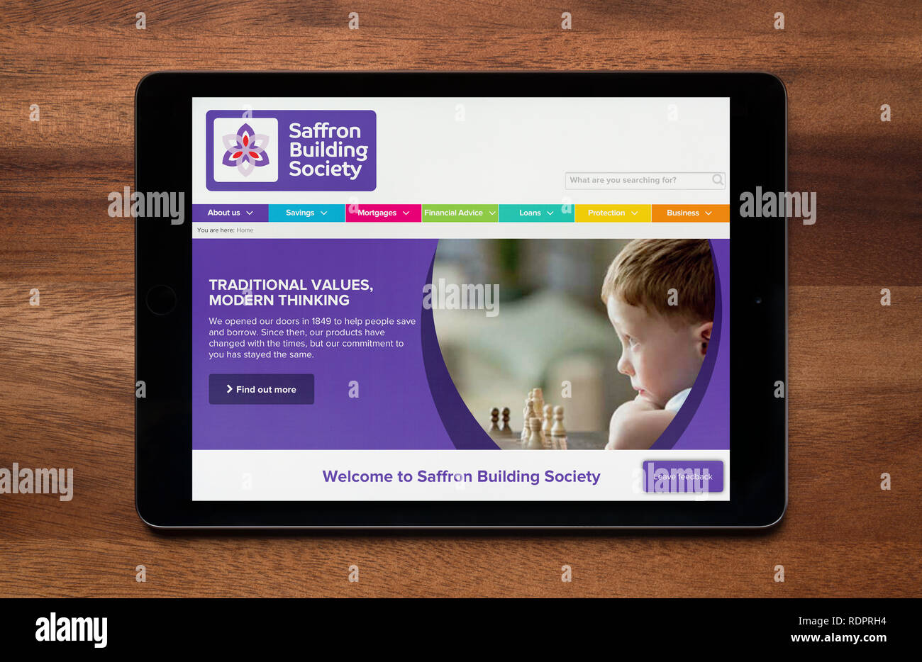 The website of Saffron Building Society is seen on an iPad tablet, which is resting on a wooden table (Editorial use only). Stock Photo