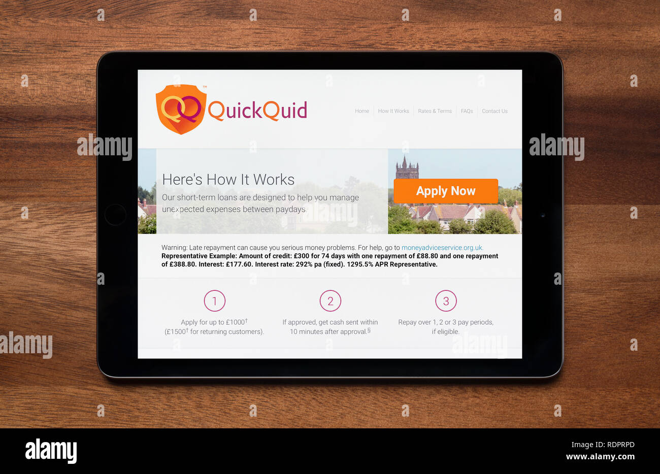 The website of QuickQuid is seen on an iPad tablet, which is resting on a wooden table (Editorial use only). Stock Photo